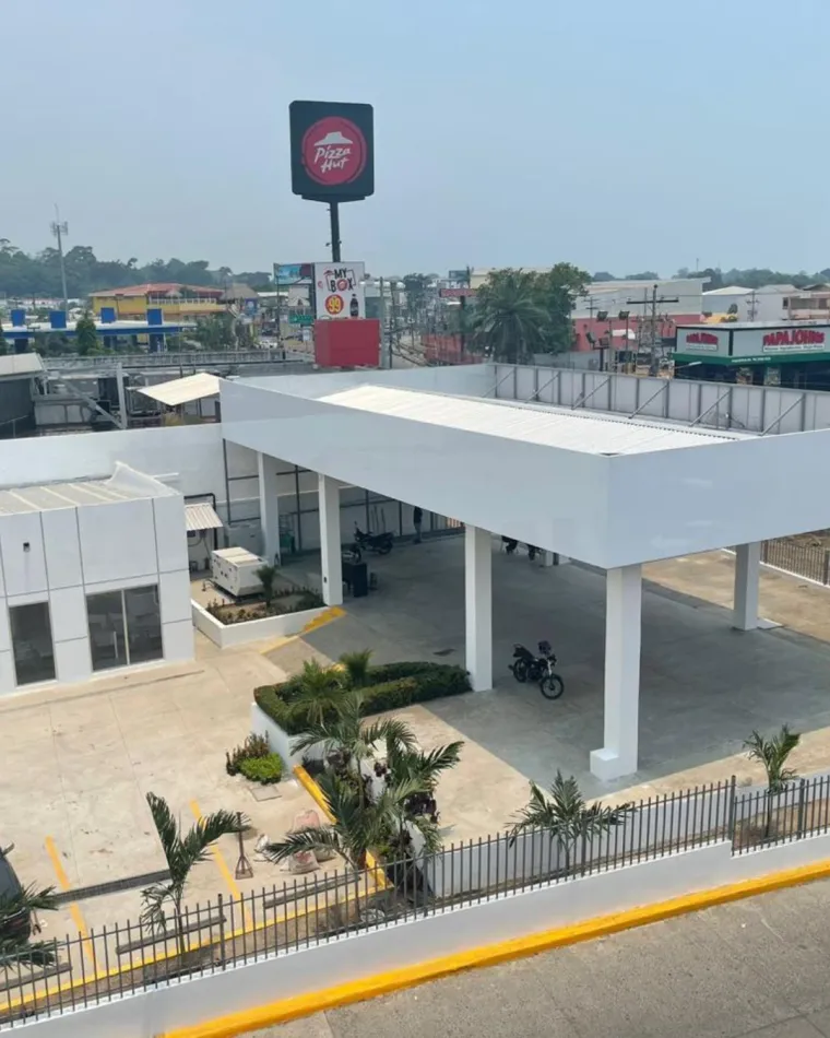 Sede terminada de AutoExcel en La Ceiba, con marquesina blanca sobre el patio y jardinera de palmeras